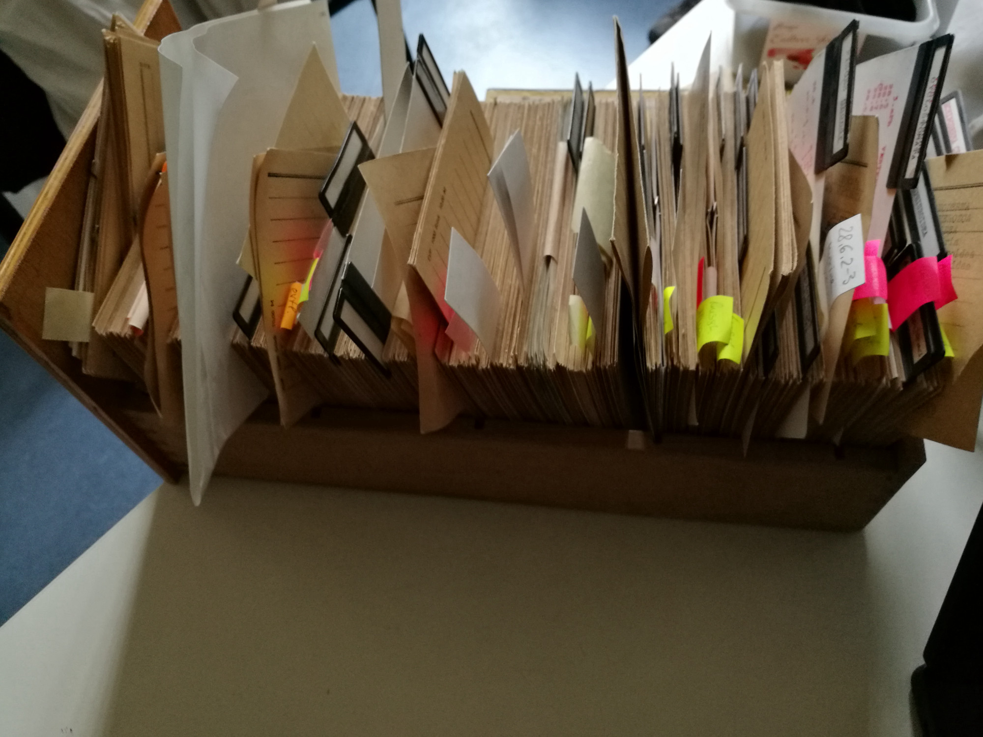 Drawer photographed from above holding hundreds of index cards lined up in the box. Some are annotated with post-its and other notes, and left to peek out, while most are tightly lined up.